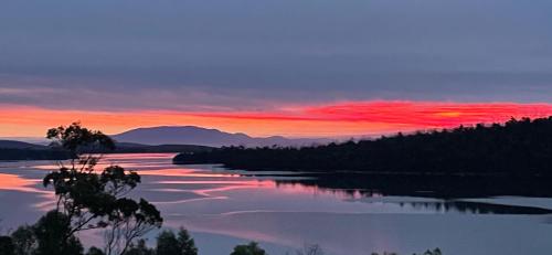 a sunset over a river with trees and mountains at The Sounds in Murdunna
