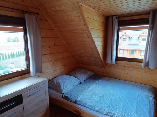 a bed in a log cabin with two windows at 4 Domki u Ewy in Ryn