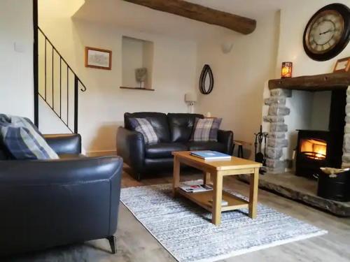 a living room with a leather couch and a fireplace at The Beautiful Bobbin - Premium Cottage with views, local walks, wood burner & pubs in Tideswell