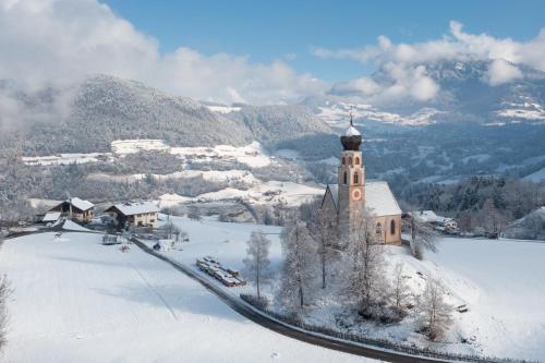 a church with a clock tower on a snow covered hill at Mesnerhof my Paradise in Fiè