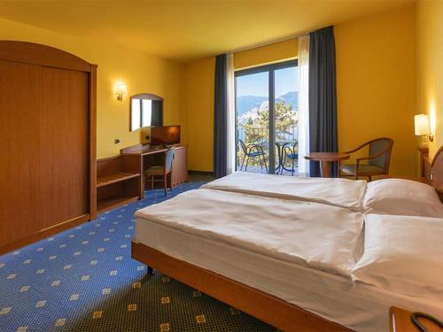 マルチェージネにあるNatur Resort Panoramaのベッド、デスク、窓が備わるホテルルームです。