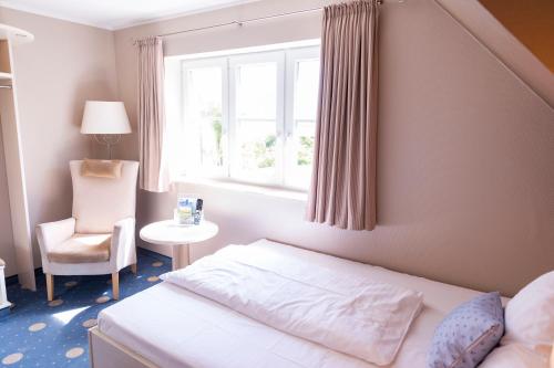 a bedroom with a bed and a chair and a window at Anker's Hörn - Hotel & Restaurant auf der Hallig Langeness in Langeneß