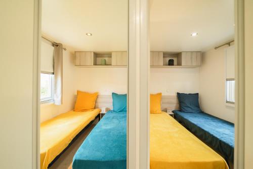 2 camas en una habitación pequeña con almohadas azules y naranjas en Mobil Home les pieds dans l'eau, en Canet-en-Roussillon