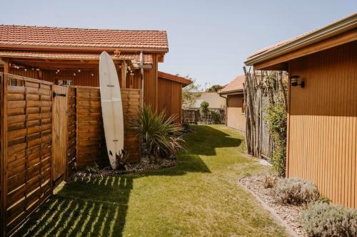 une planche de surf penchée contre une clôture à côté d'une maison dans l'établissement Villa Cocotte classée 4 étoiles à 150 m de la plage 4 chambres, à Biscarrosse-Plage