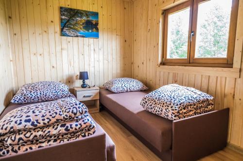 two beds in a room with wooden walls and a window at Domek Bieszczady Jezioro Solińskie in Wołkowyja