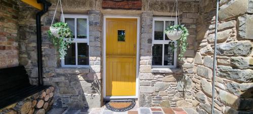 a yellow door on a stone house with two windows at Frontview Cottage - Two Bedroom - Sleeps 6 guests in Ballynahinch