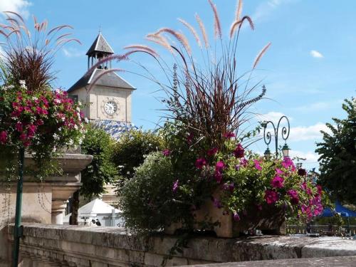 a building with a clock tower in the background with flowers at Maison Calme au Cœur du Périgord Noir - 3 Chambres in Le Bugue