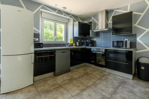 een keuken met zwarte kasten en een witte koelkast bij Village house 3 bedrooms large terrace - Dodo et Tartine in Villedieu-les-Poëles