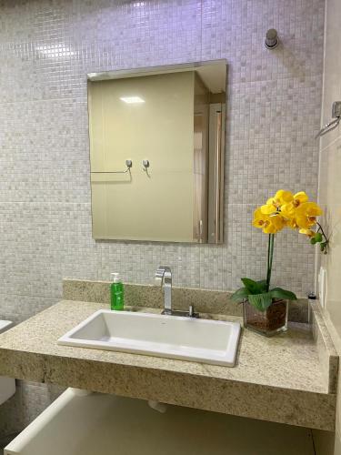a bathroom sink with a mirror and a vase of yellow flowers at Apartamento confortável, localização extra -recepção 24h- Varanda com vista panorâmica in Juazeiro do Norte
