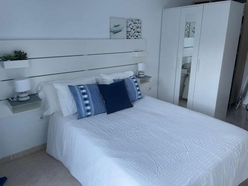 Dormitorio blanco con cama blanca y almohadas azules en Espacio tranquilo cerca del mar, en Santa Cruz de Tenerife