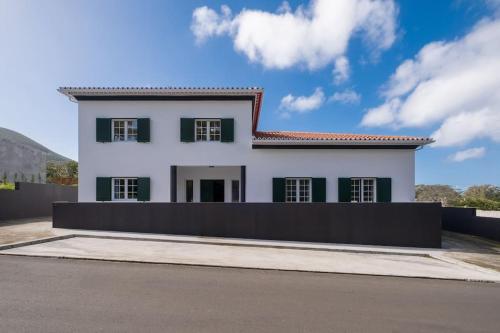 a white house with green shuttered windows at Batalha Family House in Fenais da Luz