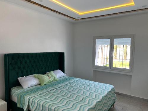 Schlafzimmer mit einem Bett mit einem grünen Kopfteil und einem Fenster in der Unterkunft VillaLina Haut Standing Djerba in Ajim
