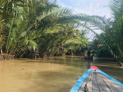 a man riding a boat down a river with palm trees at Ba Danh Homestay & Kitchen - Ben Tre Mekong in Ben Tre