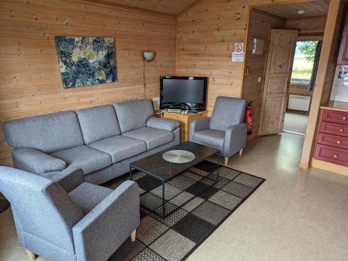 uma sala de estar com um sofá e duas cadeiras e uma televisão em Solstrand Camping em Vigeland