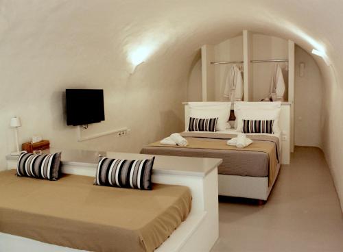 a bedroom with two beds and a tv on the wall at OUTOPOIA CAVE STUDIOS in Oia