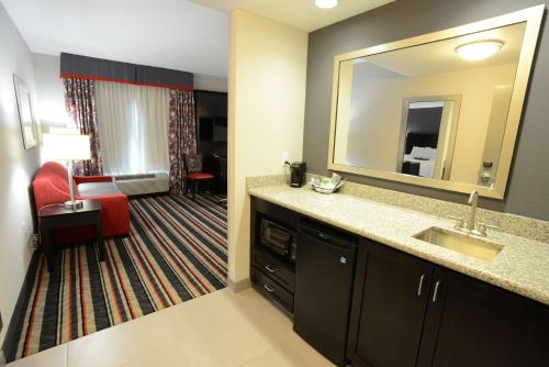 ein Badezimmer mit einem Waschbecken und einem Spiegel sowie ein Wohnzimmer in der Unterkunft Hampton Inn & Suites Albany at Albany Mall in Albany