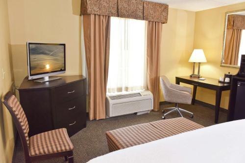 アレクサンドリアにあるHampton Inn & Suites Alexandriaのベッド、テレビ、椅子が備わるホテルルームです。