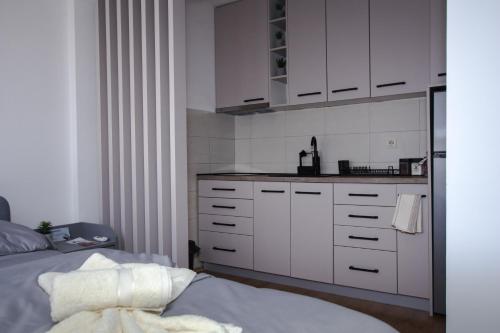 a white kitchen with white cabinets and a bed at Apartman 21 in Kraljevo