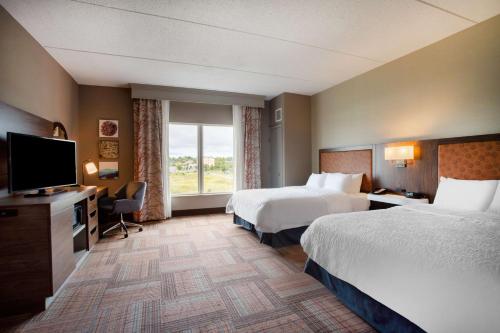 a hotel room with two beds and a flat screen tv at Hampton Inn Watertown in Watertown