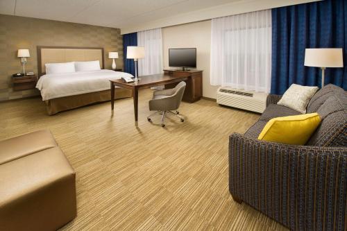 Hampton Inn & Suites Baltimore/Woodlawn في بالتيمور: غرفة الفندق بسرير ومكتب واريكة