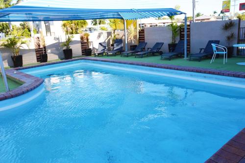 a swimming pool with a blue umbrella and chairs at Rover Motel in Mackay