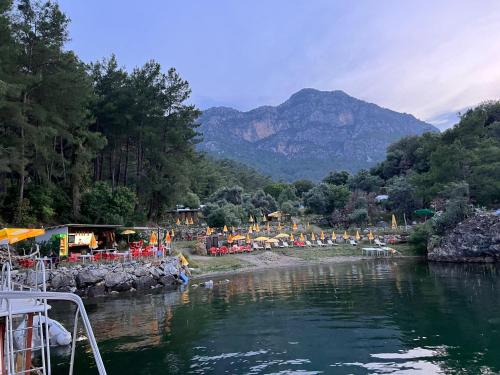 a river with a group of tables and chairs next to a mountain at Sultaniye Camping in Mugla