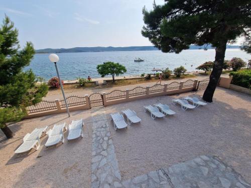 a group of lounge chairs and a tree and water at 5 meters FROM THE SEA with private beach - 70m2 Colibri Sunset Apartments in Sveti Petar
