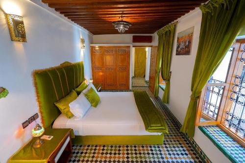 a bedroom with a bed with green curtains and a window at Riad Sahraui in Fès