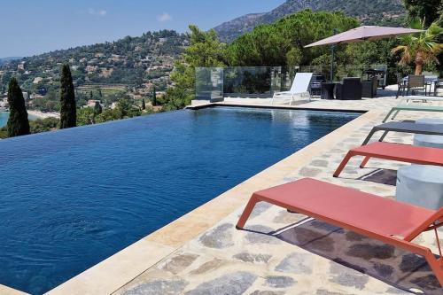 a swimming pool with two red chairs and a swimming pool at Splendide villa vue mer 180° à 500 m de la plage in Le Lavandou