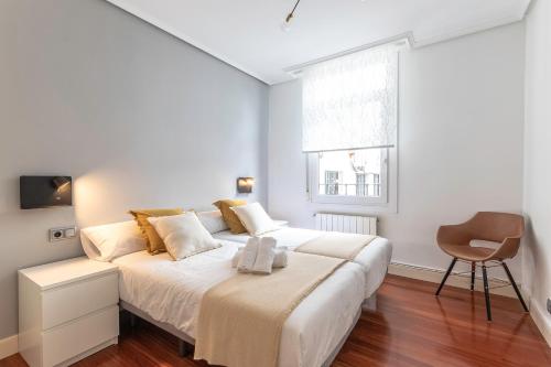 a white bedroom with a bed and a chair at Apartamento La Alameda de Indautxu in Bilbao