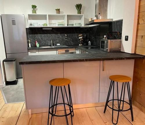 une cuisine avec deux tabourets de bar et un comptoir dans l'établissement Le Bon appart, à Marlens