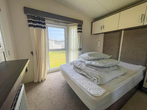 a bedroom with a bed with pillows and a window at Beautiful 8 Berth Caravan With Decking At Broadland Sands In Suffolk Ref 20017cv in Hopton on Sea