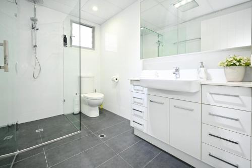 a white bathroom with a shower and a sink and a toilet at Stylish 2 b/r apartment - 4 guests, garage ZC5 in Alexandra Headland
