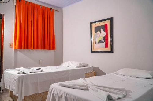 two beds in a room with an orange curtain at Pousada Sol de Verão in Barra do Garças