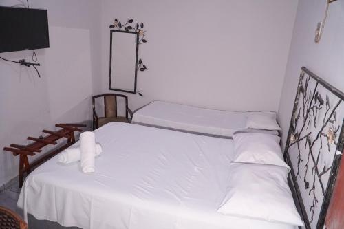 a bedroom with a bed with white sheets and a mirror at Pousada Sol de Verão in Barra do Garças