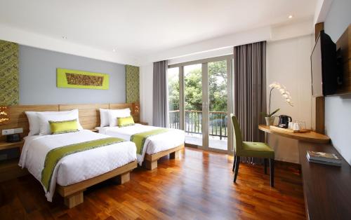 a hotel room with two beds and a desk and a window at d'primahotel Petitenget Seminyak 2 in Seminyak