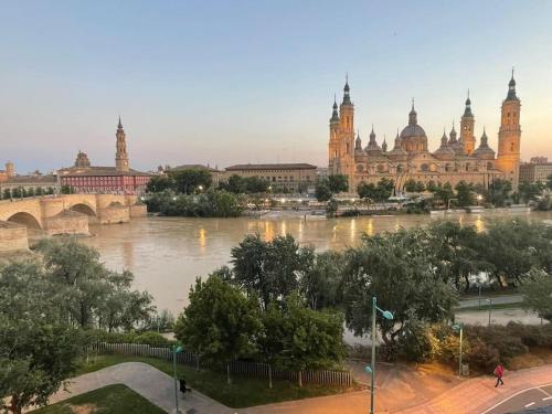 a river in front of a large building with a bridge at Apartamento Con Vistas Al Pilar con Aparcamiento privado in Zaragoza