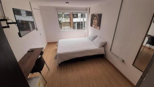 Habitación pequeña con cama y escritorio. en Apartaestudios Amoblados Galerías, en Bogotá