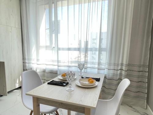 uma mesa de jantar com cadeiras brancas e uma janela em Апартаменты Freedom Greenline Сыганак Хан Шатыр em Taldykolʼ