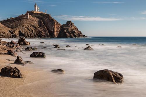 a beach with a lighthouse on top of a mountain at Hotel Calachica Las Negras in Las Negras