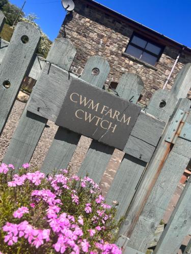 een bord aan de zijkant van een gebouw met roze bloemen bij Cwm Farm Cwtch in Merthyr Tydfil