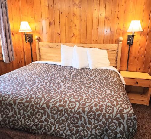 a bed in a room with wooden walls and two lamps at Canyon Motel in Hot Sulphur Springs