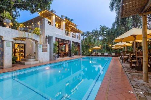 a swimming pool with tables and umbrellas next to a house at Baanpong Lodge in San Kamphaeng