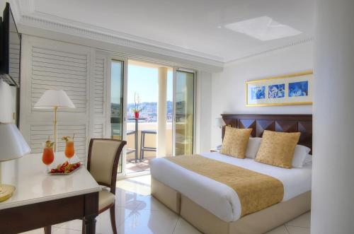 a bedroom with a bed and a desk and a table and chair at Hôtel West End Promenade in Nice