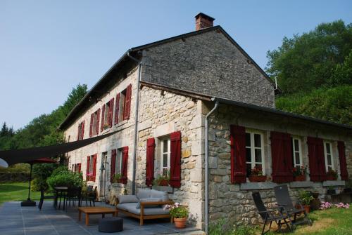 um antigo edifício de pedra com janelas com persianas vermelhas em Le Moulin de la Farge B&B em Saint-Moreil