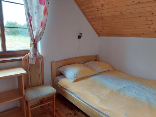 a bedroom with a bed and a chair and a window at Domki nad jeziorem - Posiadłość Nad Zatoką in Ryn
