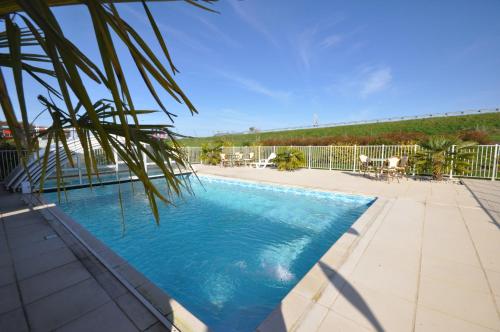 una piscina con una palmera en el primer plano en The Originals City, Hôtel Alexia, La Souterraine (Inter-Hotel), en La Souterraine