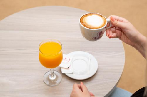 a person holding a cup of coffee and a glass of orange juice at Casino Motel Senator in Gevgelija