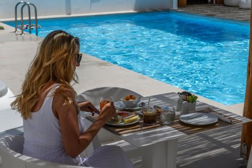 una mujer sentada en una mesa con una comida junto a una piscina en Mykonaki Hotel en Ano Mera