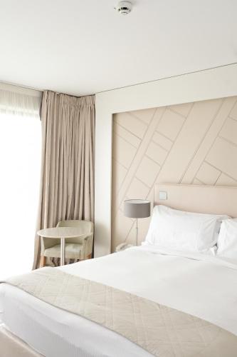a white bedroom with a bed and a chair at Thalazur Cabourg - Hôtel & Spa in Cabourg